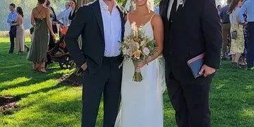 A bride and groom standing with their officiant, Pastor Dave, outdoors after a wedding ceremony.