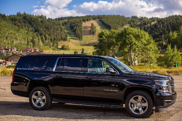 A black Chevrolet Suburban SUV with Snow Country Limousine branding parked in a mountainous area.