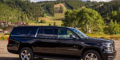 A black Chevrolet Suburban SUV with Snow Country Limousine branding parked in a mountainous area.