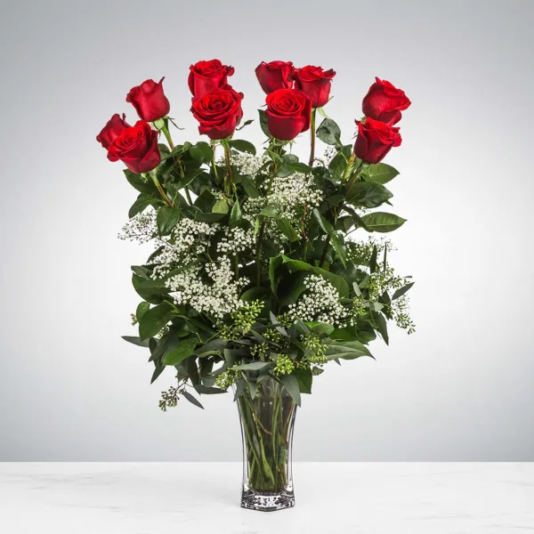 A tall bouquet of red roses with white baby's breath filler in a clear glass vase.