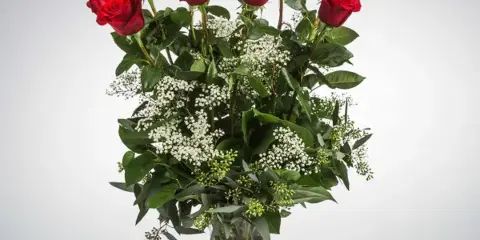 A tall bouquet of red roses with white baby's breath filler in a clear glass vase.