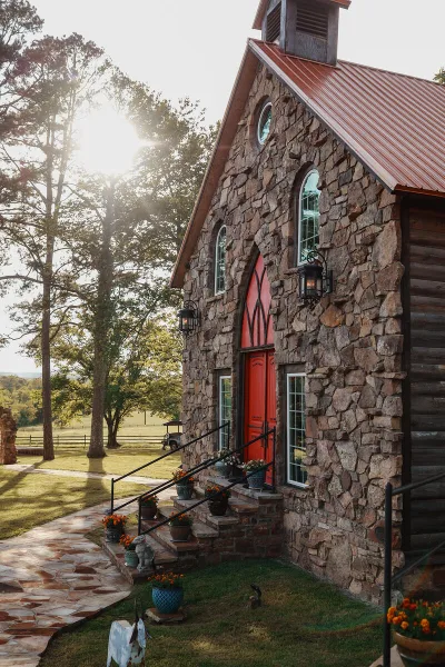 Exterior view of a historic stone chapel with a red door and copper roof, surrounded by trees and a stone pathway.