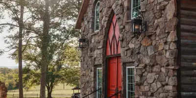Exterior view of a historic stone chapel with a red door and copper roof, surrounded by trees and a stone pathway.