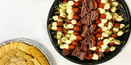 A catering spread featuring a charcuterie board with meats and cheese, a platter of tortilla pinwheels, and a tray of assorted crackers.