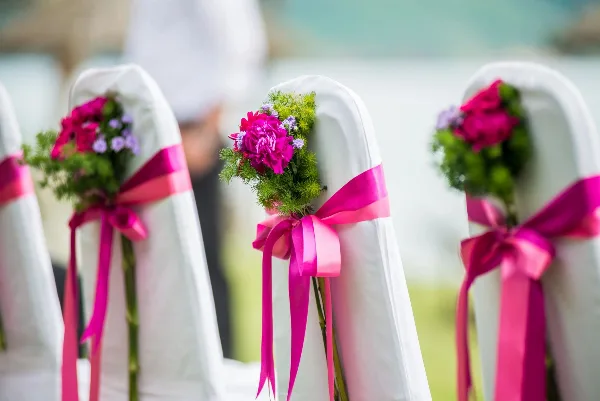 White wedding chairs decorated with pink ribbons and floral arrangements