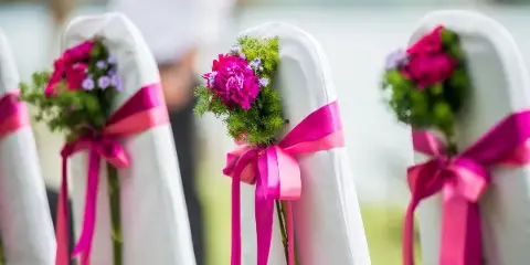 White wedding chairs decorated with pink ribbons and floral arrangements