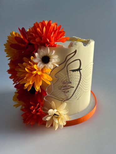A white cake decorated with vibrant orange and yellow flowers and an artistic face design.