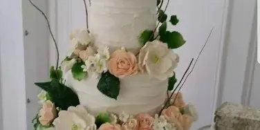 A three-tiered white wedding cake decorated with cream and peach roses, greenery, and a framed silhouette topper.
