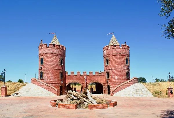 Exterior view of the Castle Noz venue featuring twin red brick towers with conical roofs, a central arched entrance, and a paved courtyard with a fire pit in the foreground.