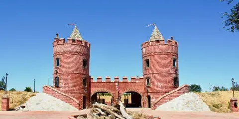 Exterior view of the Castle Noz venue featuring twin red brick towers with conical roofs, a central arched entrance, and a paved courtyard with a fire pit in the foreground.