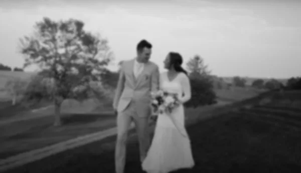 Black and white photograph of a bride and groom standing together outdoors in a field.