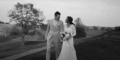 Black and white photograph of a bride and groom standing together outdoors in a field.