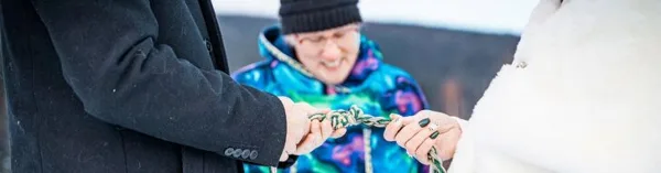 A close-up of a handfasting ceremony where a couple's hands are tied with a rope by an officiant in a snowy outdoor setting.