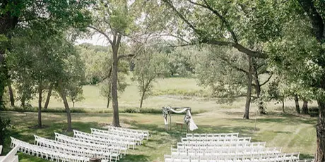 An outdoor wedding ceremony setup featuring rows of white chairs and a decorated altar under trees.