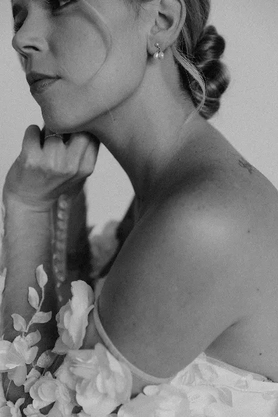 A black and white close-up profile of a bride showing a polished low bun hairstyle and pearl earrings.