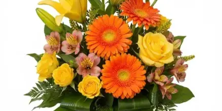 A floral arrangement featuring yellow lilies, orange gerbera daisies, and yellow roses in a clear glass vase.