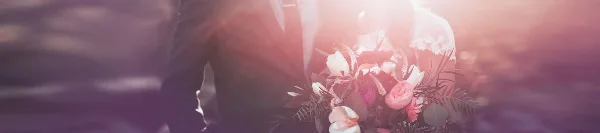 A close-up of a bride and groom holding a large, mixed wedding bouquet with pink and white flowers and greenery.