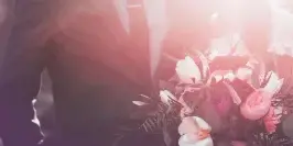 A close-up of a bride and groom holding a large, mixed wedding bouquet with pink and white flowers and greenery.