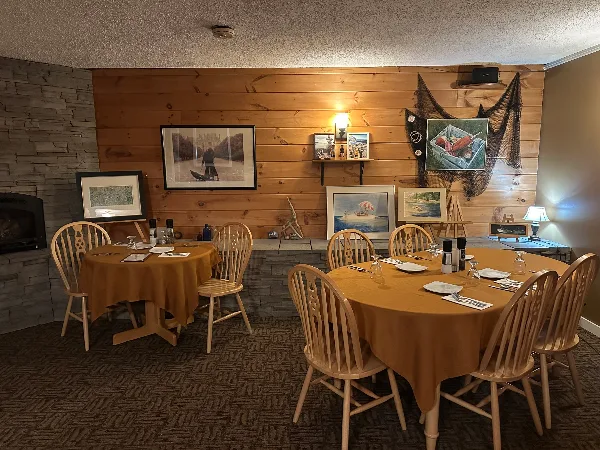 Interior view of a restaurant dining room with wooden tables, chairs, and framed artwork on the walls.