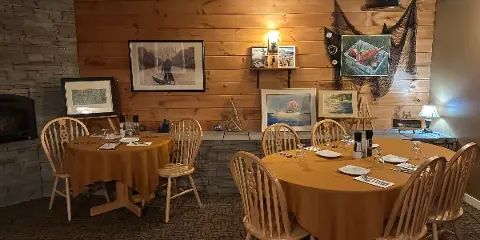 Interior view of a restaurant dining room with wooden tables, chairs, and framed artwork on the walls.