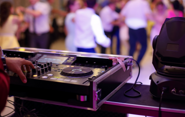 A DJ's hands operating a turntable and mixer at a live event with a crowd dancing in the background.