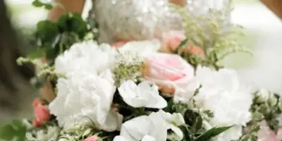 A close-up of a bride holding a large, romantic bouquet of white and pink flowers with greenery.