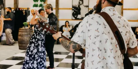 A couple dancing at a wedding reception while a musician plays guitar in the foreground.