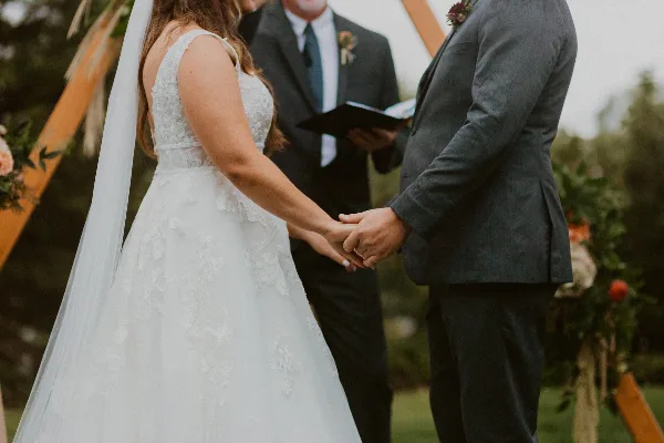 A bride and groom holding hands during an outdoor wedding ceremony with an officiant in the background.