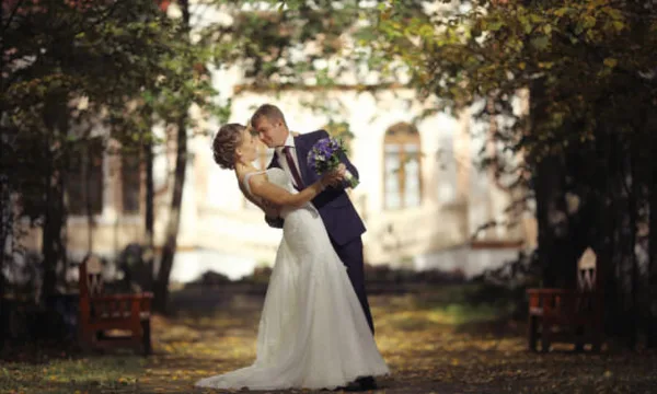 A bride and groom embracing and kissing in a garden setting.