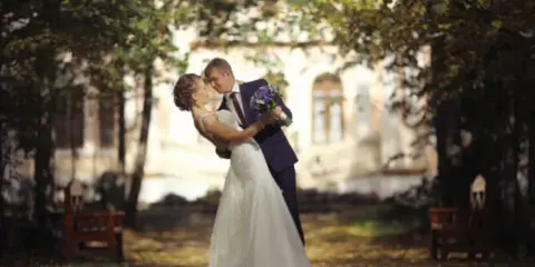 A bride and groom embracing and kissing in a garden setting.
