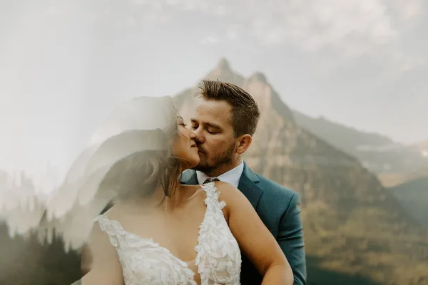 A bride and groom sharing a kiss with a mountain peak in the background.