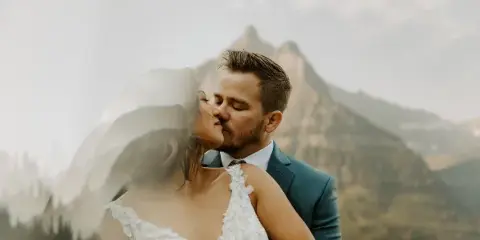 A bride and groom sharing a kiss with a mountain peak in the background.