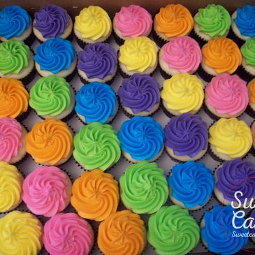A close-up view of a tray filled with numerous cupcakes decorated with vibrant, multi-colored frosting swirls.