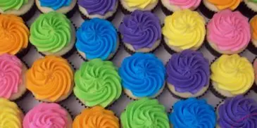 A close-up view of a tray filled with numerous cupcakes decorated with vibrant, multi-colored frosting swirls.