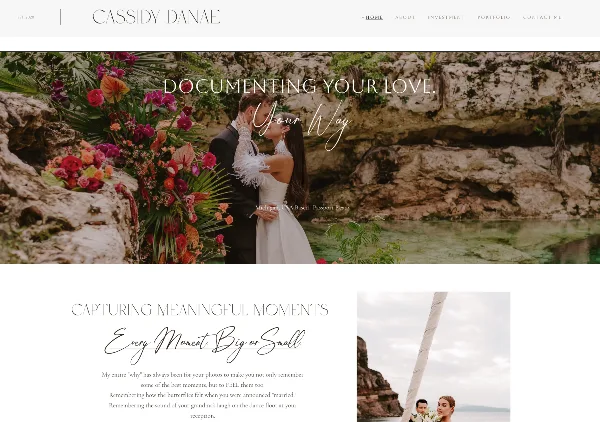 A bride and groom kissing in front of a lush floral arrangement and rocky coastal scenery.