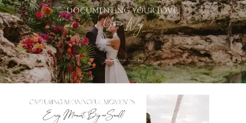 A bride and groom kissing in front of a lush floral arrangement and rocky coastal scenery.