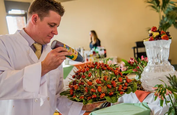 A chef in a white coat garnishing a large appetizer display with toothpicks at a catering event.