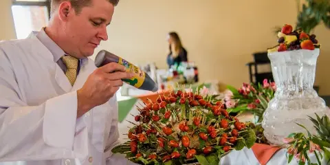 A chef in a white coat garnishing a large appetizer display with toothpicks at a catering event.
