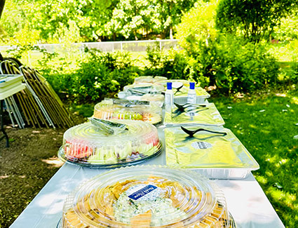 Outdoor catering table set with multiple covered food trays and platters.