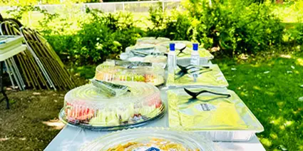 Outdoor catering table set with multiple covered food trays and platters.