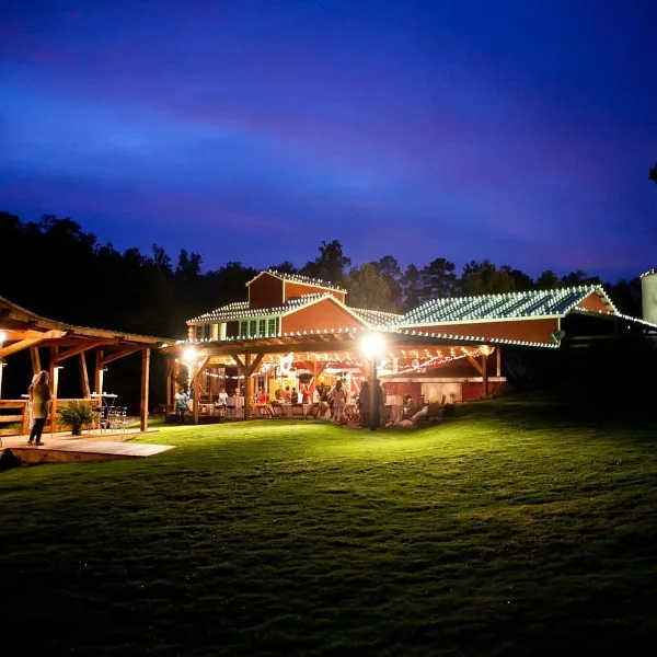 Nighttime view of the Yellowleaf Creek Mill venue featuring a historic building and a covered outdoor reception area illuminated by string lights with guests present.