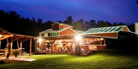 Nighttime view of the Yellowleaf Creek Mill venue featuring a historic building and a covered outdoor reception area illuminated by string lights with guests present.