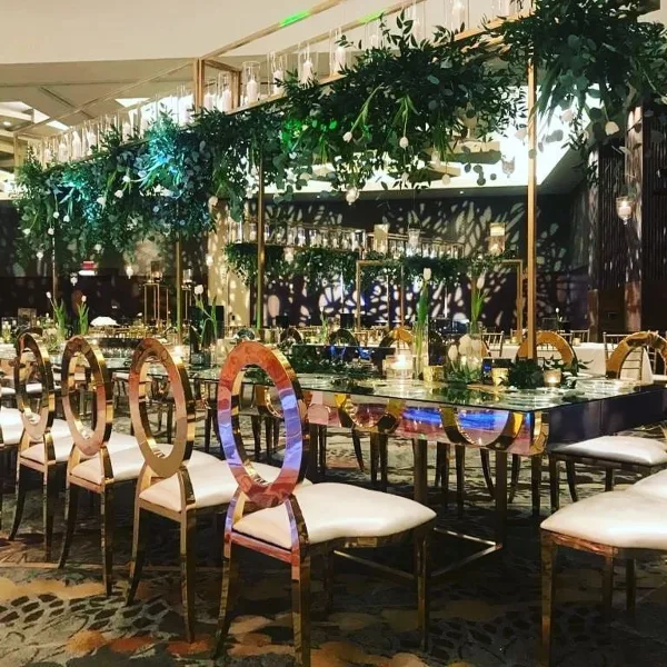 Luxury event decor featuring mirrored chairs, glass tables, and floral installations in a banquet hall.