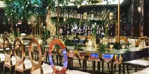 Luxury event decor featuring mirrored chairs, glass tables, and floral installations in a banquet hall.
