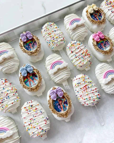 Decorated white dessert pops with colorful sprinkles, bows, and edible picture details.
