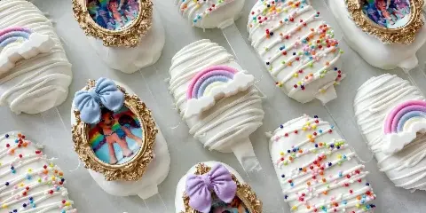 Decorated white dessert pops with colorful sprinkles, bows, and edible picture details.