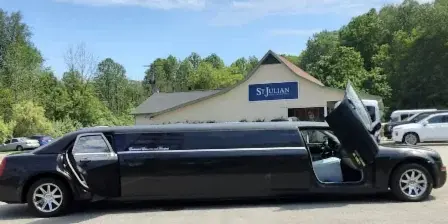A black stretch limousine with company branding parked in a lot with a building in the background.