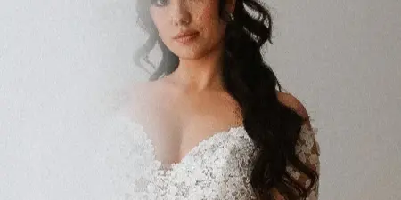 A bride wearing a white lace wedding dress with professionally styled wavy hair and full makeup.