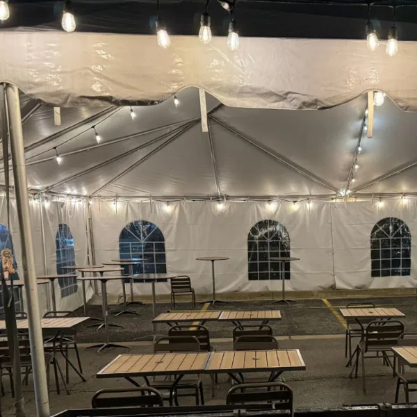 Interior of a white event tent set up with tables, chairs, and string lights.