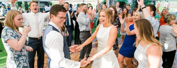 A bride and groom dancing at a wedding reception while surrounded by cheering guests.